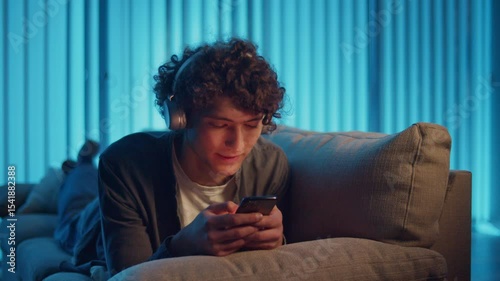 Digital Detox, Mental Health, Focus Mode. Man Relaxes on Sofa Scrolling Phone, Possibly Listening a Podcast or Browsing. Everyday Self-Care and Slow Living in the Digital Age