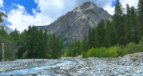 Fotografie Turquoise wild alpine river winds through rocky riverbed beneath towering peaks and green coniferous trees
