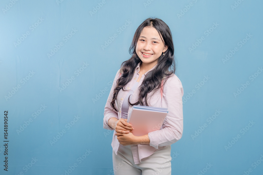 Fototapeta premium A woman is holding a book and a backpack. She is smiling and looking at the camera. Concept of confidence and readiness, as the woman is prepared for her day ahead
