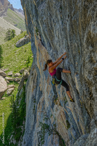 Strong, agile woman caught in the middle of climbing an overhanging rock face, demonstrating impressive skill and focus. Challenging and adventurous nature of outdoor rock climbing in alpine world.