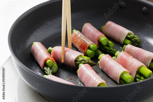 フライパンでアスパラベーコンを焼く料理のシーン　Asparagus Bacon Being Cooked in a Frying Pan