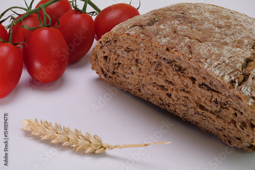 Primo piano di pagnotta integrale, spiga di grano e pomodorini sul tavolo