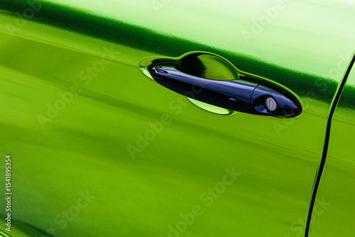 A vibrant, close-up shot of a sleek black car door handle against a striking metallic green car body