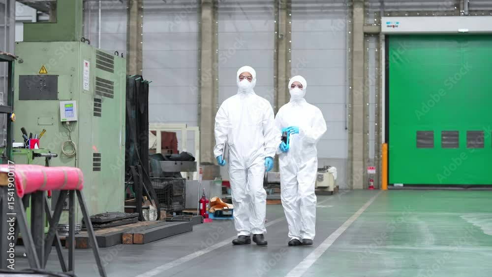Male and female workers in protective clothing walking through a factory Male and female workers in protective clothing walking through a factory