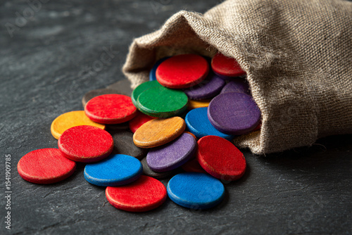 Colorful wooden tokens spill from a burlap sack onto a dark surface during a game night gathering in a cozy setting