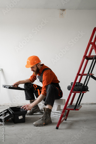 Male repairer. Handyman concept. Man in overalls opening toolbox sitting on ladder.