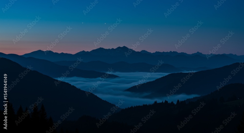 Obraz premium Mountain range silhouette captured at blue hour, layers of mist rolling between valleys