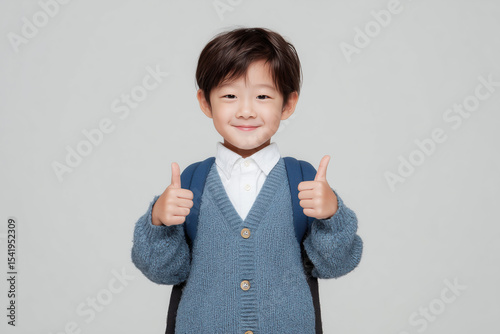 primary school kid with a backpack and thumbs up on neutral studio background