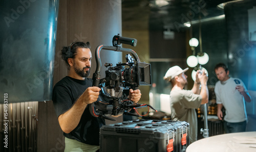 Director of photography with a camera in his hands on the set. Professional videographer at work on filming a movie, commercial or TV series. Filming process indoors, studio