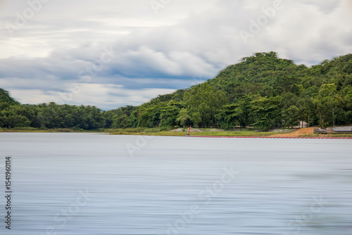 A peaceful rural scene in the dam featuring a yellow meadow and green mountain with blue sky, Chachoengsao, Thailand.