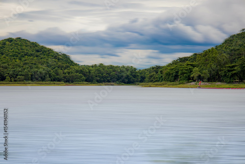 A peaceful rural scene in the dam featuring a yellow meadow and green mountain with blue sky, Chachoengsao, Thailand.