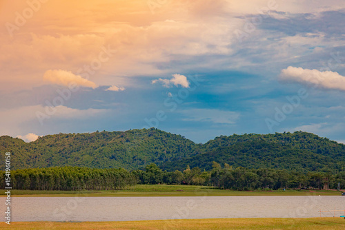 A peaceful rural scene in the dam featuring a yellow meadow and green mountain with blue sky, Chachoengsao, Thailand.