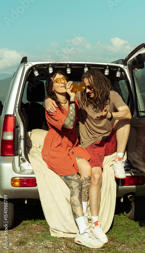 Wallpaper Mural Smiling couple sitting in car trunk, drinking from bottle and enjoying mountain road trip adventure on a sunny day. Torontodigital.ca