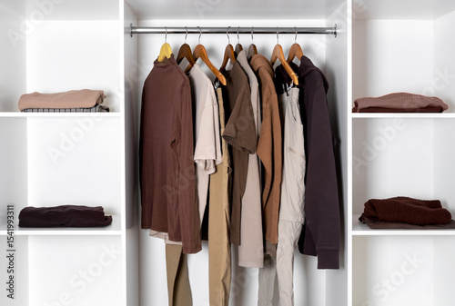 Wallpaper Mural Minimalist wardrobe with neutral-toned clothing on hangers and folded garments on white shelves. Organized and stylish modern closet design. Torontodigital.ca