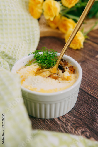 Single serving baked egg dish in baking cup, decorated with dill in a warm color combination with roses on the wooden surface for food blogging, recipe and blog post
