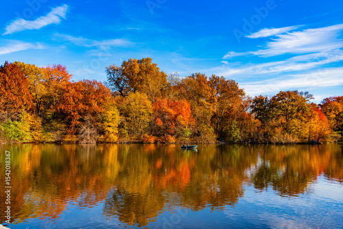 Central Park Lake in autumn with people rowing boat. Central Park on sunny autumn day change colors. Autumn landscape. Fall nature. Rowboat on a small lake at the Central Park. Boating