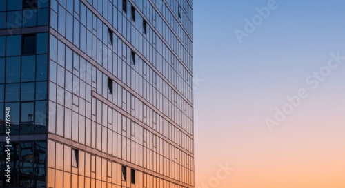 A close-up, low-angle view of a modern glass skyscraper reflecting the warm tones of a sunset or sunrise sky, symbolizing contemporary urban architecture.