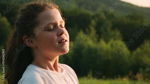 Portrait of happy preteen girl opens eyes and enjoy nature during warm summer sunset. Dreamy peaceful relaxed smiling child breathing fresh air. Childhood and weekend concept. Slow motion
