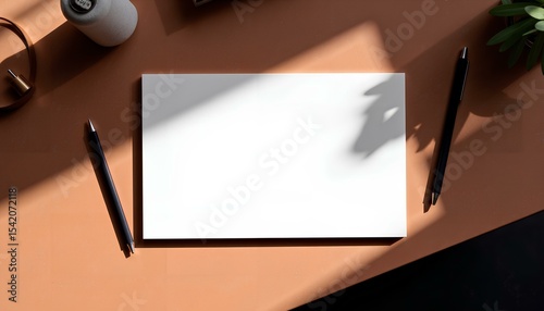 Flat lay with white paper, coffee, and stationery on terracotta desk, natural light shadows.