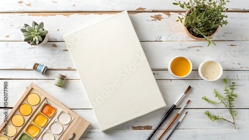 Blank canvas mockup with watercolor paints and brushes on white wooden table