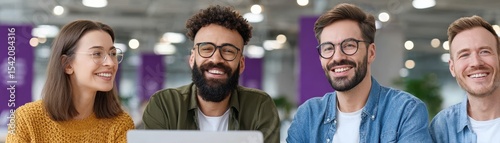 Four diverse young professionals smiling together in a modern office space, collaborating on a project with a laptop.