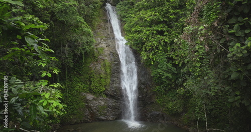 Pure freshwater waterfall cascading down a rocky cliff surrounded by lush green vegetation in a green tropical rainforest, creating a tranquil natural landscape. Amazing nature travel background
