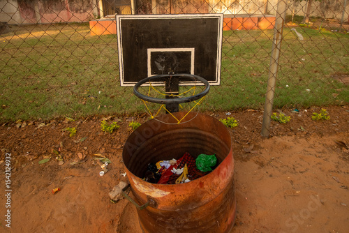 Rusty Recycle Bin with Makeshift Basketball Backboard on Dirt Ground – Creative Waste Disposal Signage