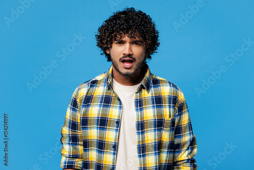 Young sad mad shocked indignant outraged dissatisfied Indian man he wears yellow checkered shirt casual clothes look camera isolated on plain blue cyan background studio portrait. Lifestyle concept.