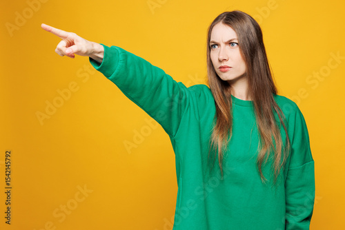 Young sad mad furious outraged Caucasian woman she wear green sweatshirt casual clothes point index finger aside scream isolated on plain yellow orange background studio portrait. Lifestyle concept.