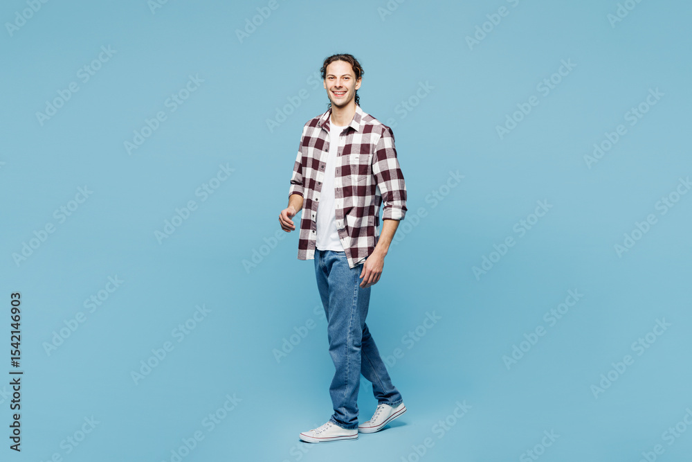 Naklejka premium Full body side profile view young smiling happy man he wear purple checkered shirt casual clothes walking going isolated on plain pastel light blue cyan background studio portrait. Lifestyle concept.