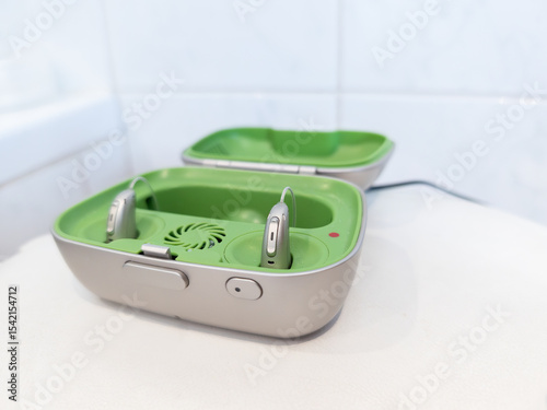 pair of modern rechargeable hearing aids placed in a green and gray charging case. Hearing devices designed for individuals with hearing loss, medical technology and senior healthcare solutions, every