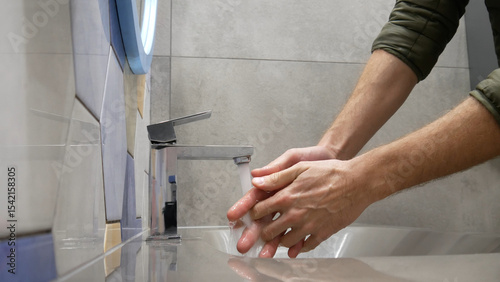 Close-up of a restroom faucet and a man washing the hands