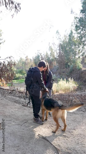 Two latin American young hikers petting their german shepherd dog during a hike in nature