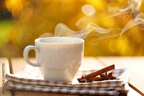 Warm steaming beverage in white mug on brown and white checkered napkin outdoors autumnal background cinnamon sticks star anise spices