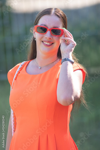 Portrait of a young beautiful girl in an orange dress in a summer forest.