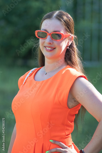 Portrait of a young beautiful girl in an orange dress in a summer forest.