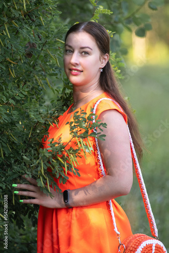 Portrait of a young beautiful girl in an orange dress in a summer forest.