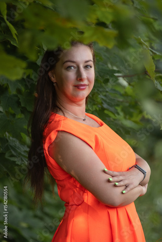 Portrait of a young beautiful girl in an orange dress in a summer forest.