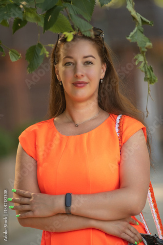 Portrait of a young beautiful girl in an orange dress in a summer forest.