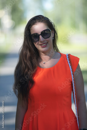 Portrait of a young beautiful girl in an orange dress in a summer forest.