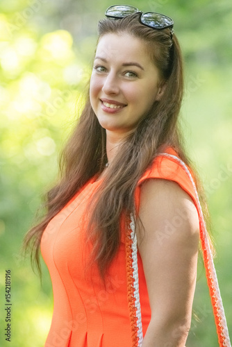Portrait of a young beautiful girl in an orange dress in a summer forest.