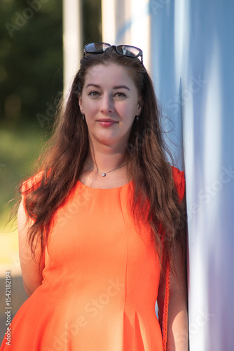 Portrait of a young beautiful girl in an orange dress in a summer forest.