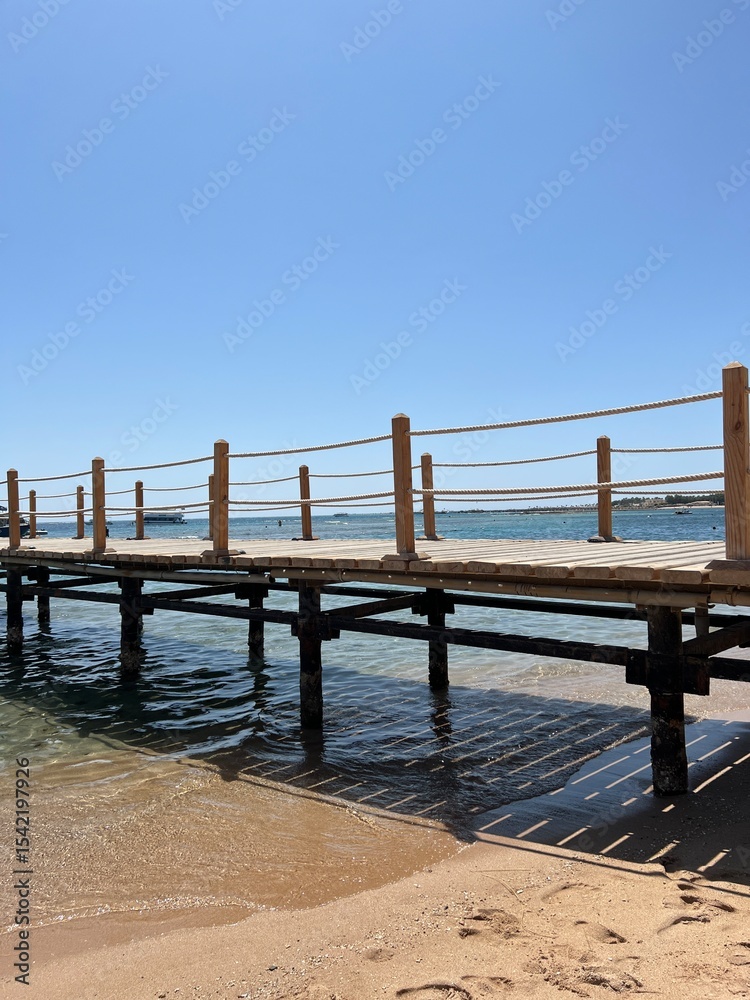 Wooden pier with a fence made of sea rope. In the background is the blue sea and clear sky Wooden pier with a fence made of sea rope. In the background is the blue sea and clear sky