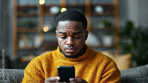 Young man in a cozy sweater focused on his smartphone in a stylish living room setting