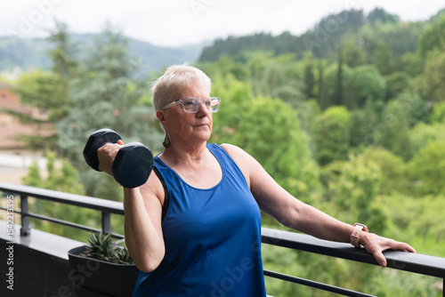 Elderly woman exercising on a home balcony with a dumbbell