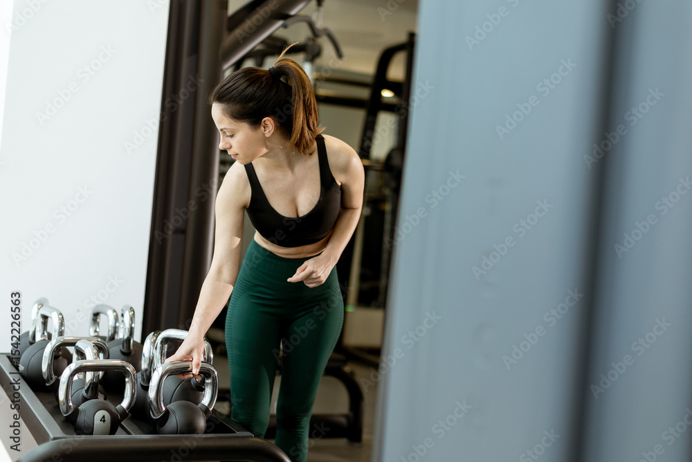 Fototapeta premium Determined athlete engages in strength training with kettlebells in a modern gym setting during morning hours