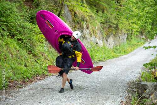 Kayaker carrying vibrant kayak along forest trail photo