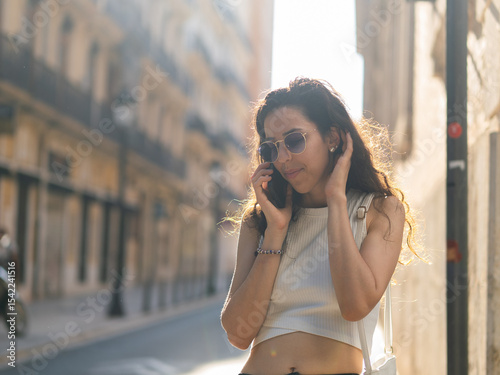 Young woman talking on phone in sunlit city street