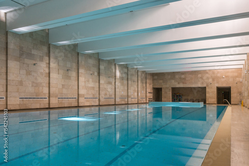 A luxurious swimming pool with walls decorated with beige tiles. A digital scoreboard has been installed. The pool is equipped with a waterfall jet.