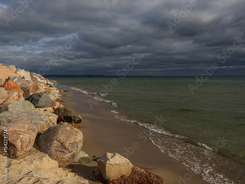 Sea. Seashore, huge rocks, sand, small waves of water and a dark cloudy sky are visible